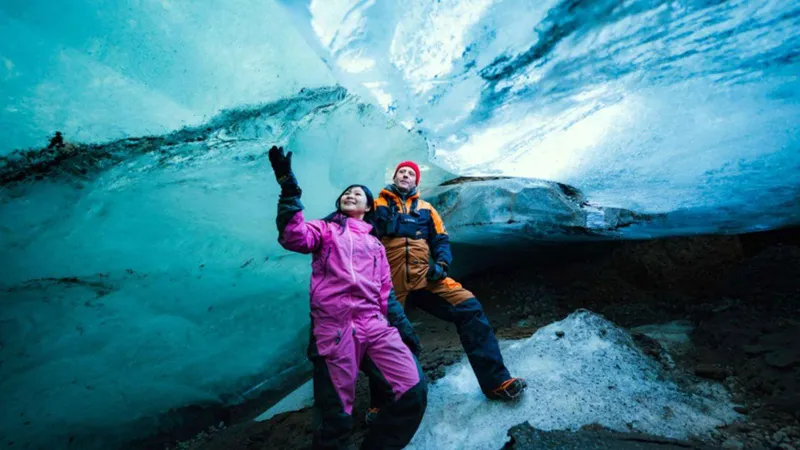 Two visitors in snowsuits inside a blue natural ice cave on a Langjökull snowmobile and ice cave tour from Geysir, Iceland