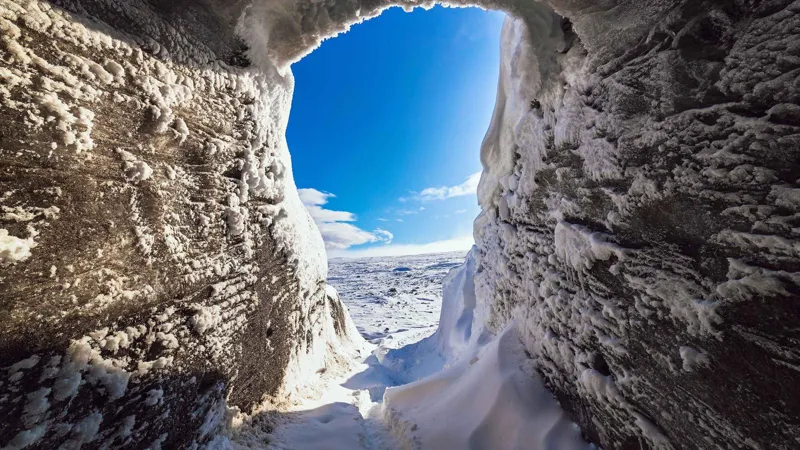 Ice cave entrance framing blue sky and the snowfield of Langjökull on an Iceland ice cave and snowmobile tour from Gullfoss